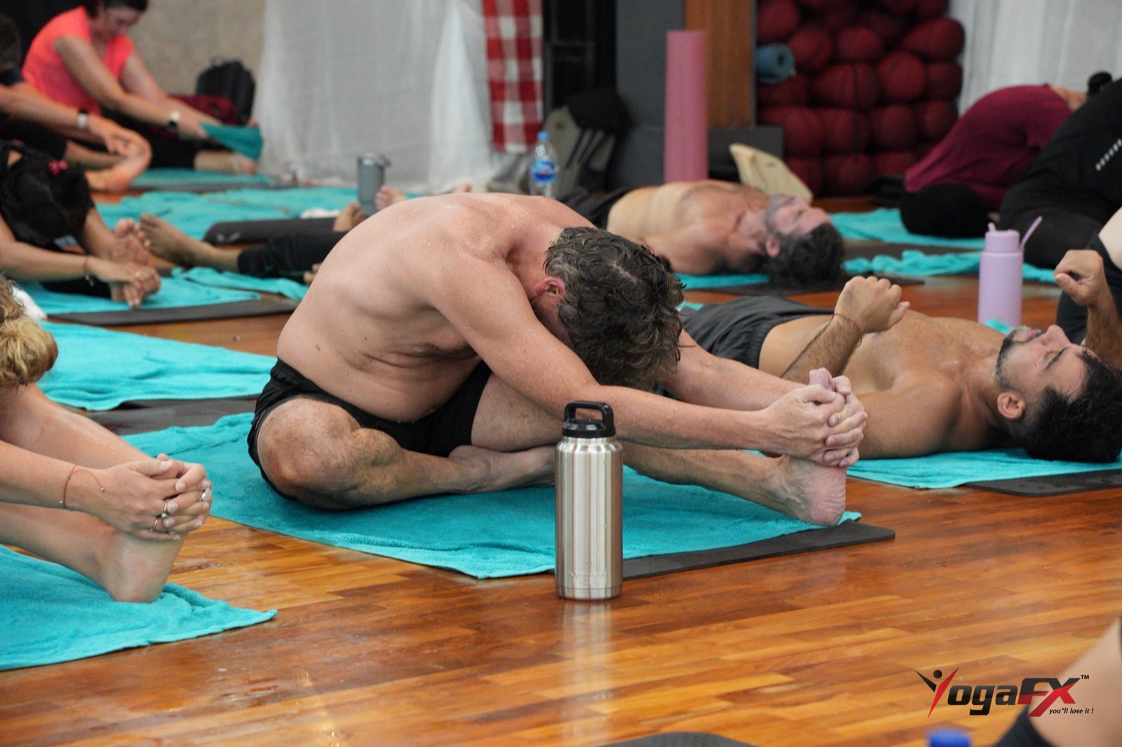 Men in a gentle seated forward fold during the floor series, the kind of soft hamstring stretch used for recovery after hard training